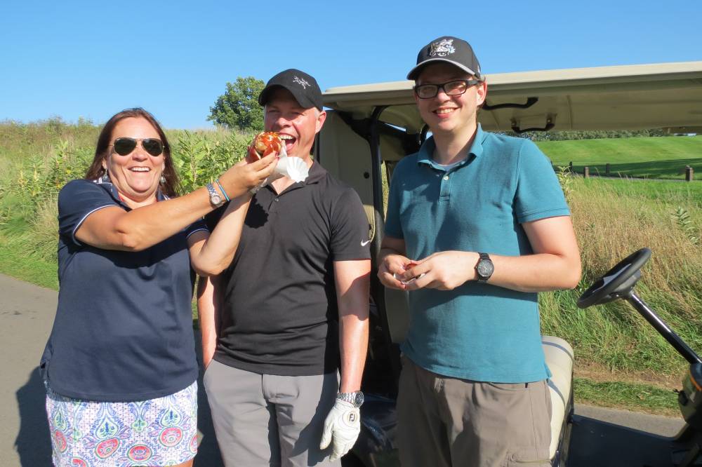 Three golfers posing for picture hotdog in face